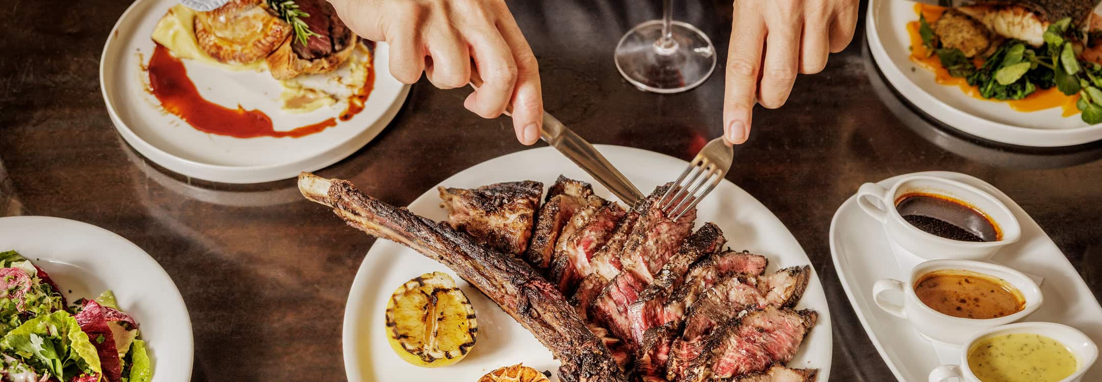 Kinsgleys tomahawk steak being carved with sauces and sides